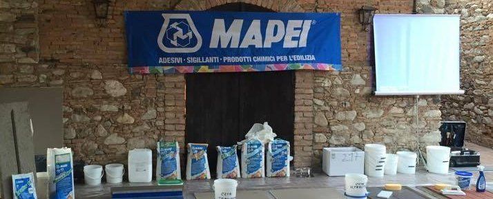 Allestimento dell'evento con striscioni Mapei e prodotti esposti su un palco, contro un muro di mattoni.