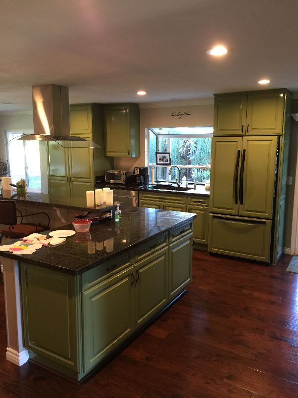 A kitchen with green cabinets, granite counter tops, stainless steel appliances and a large island