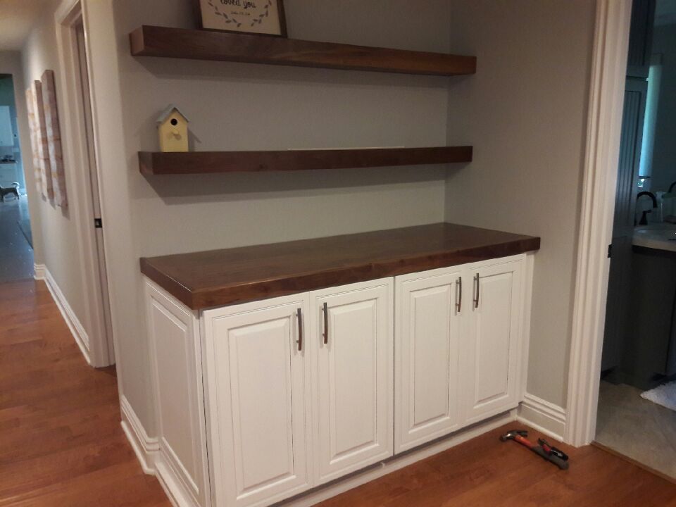 A hallway with white cabinets and wooden shelves