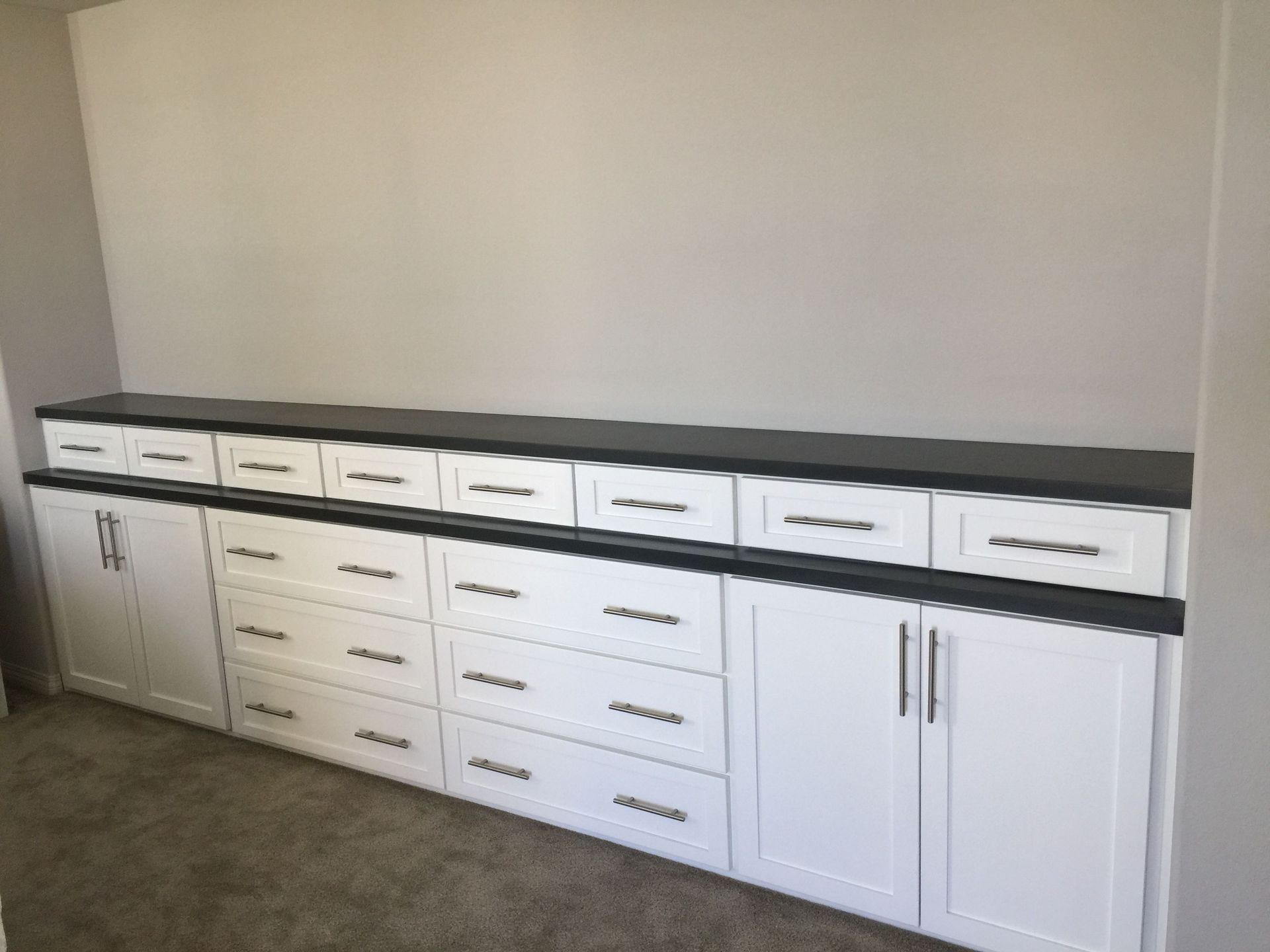A kitchen with white cabinets and drawers and a black counter top