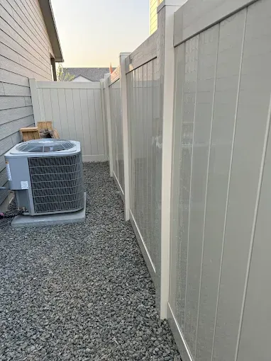 An air conditioner is sitting next to a white fence.
