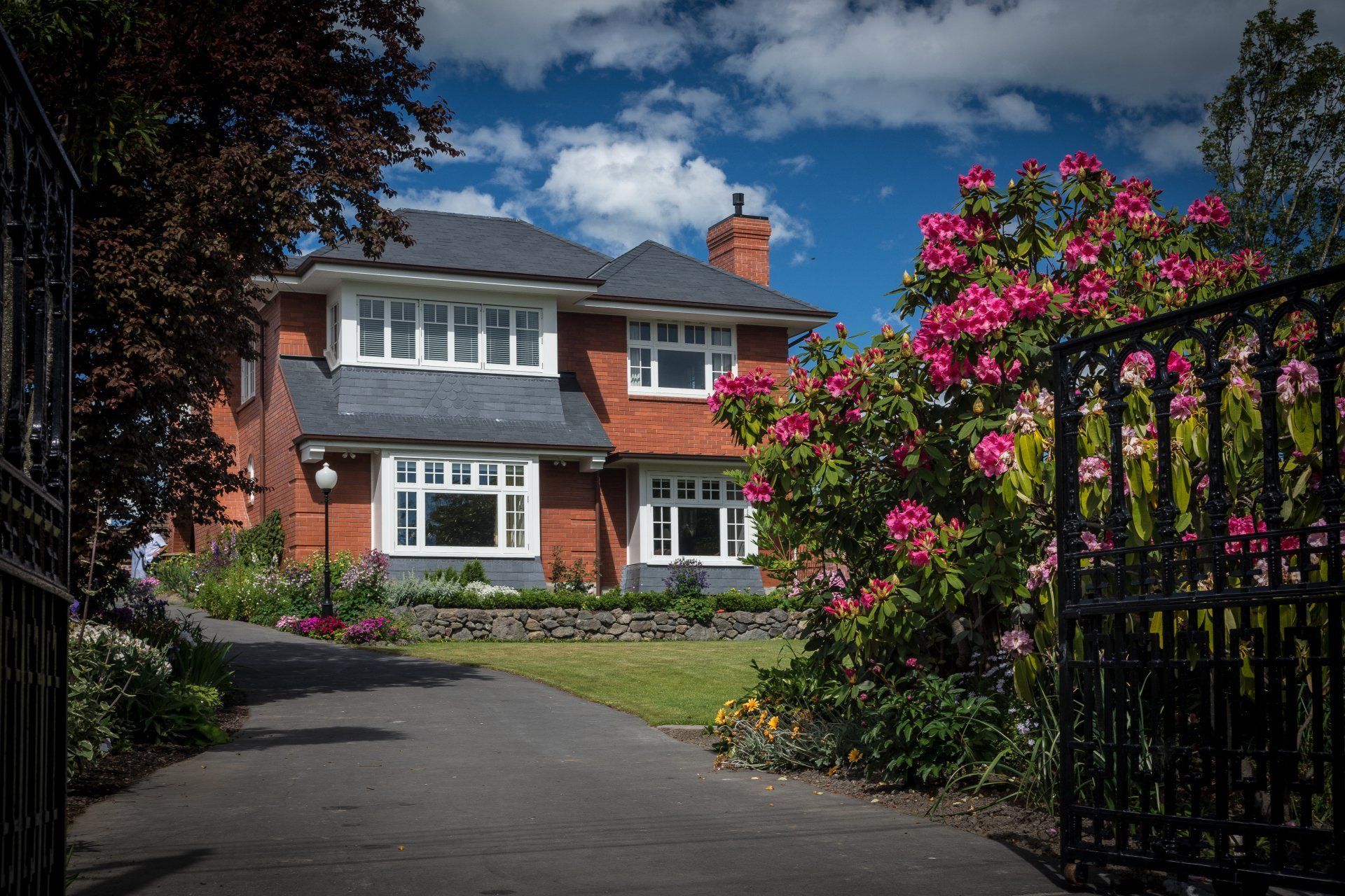 A large brick house with a driveway and flowers in front of it.