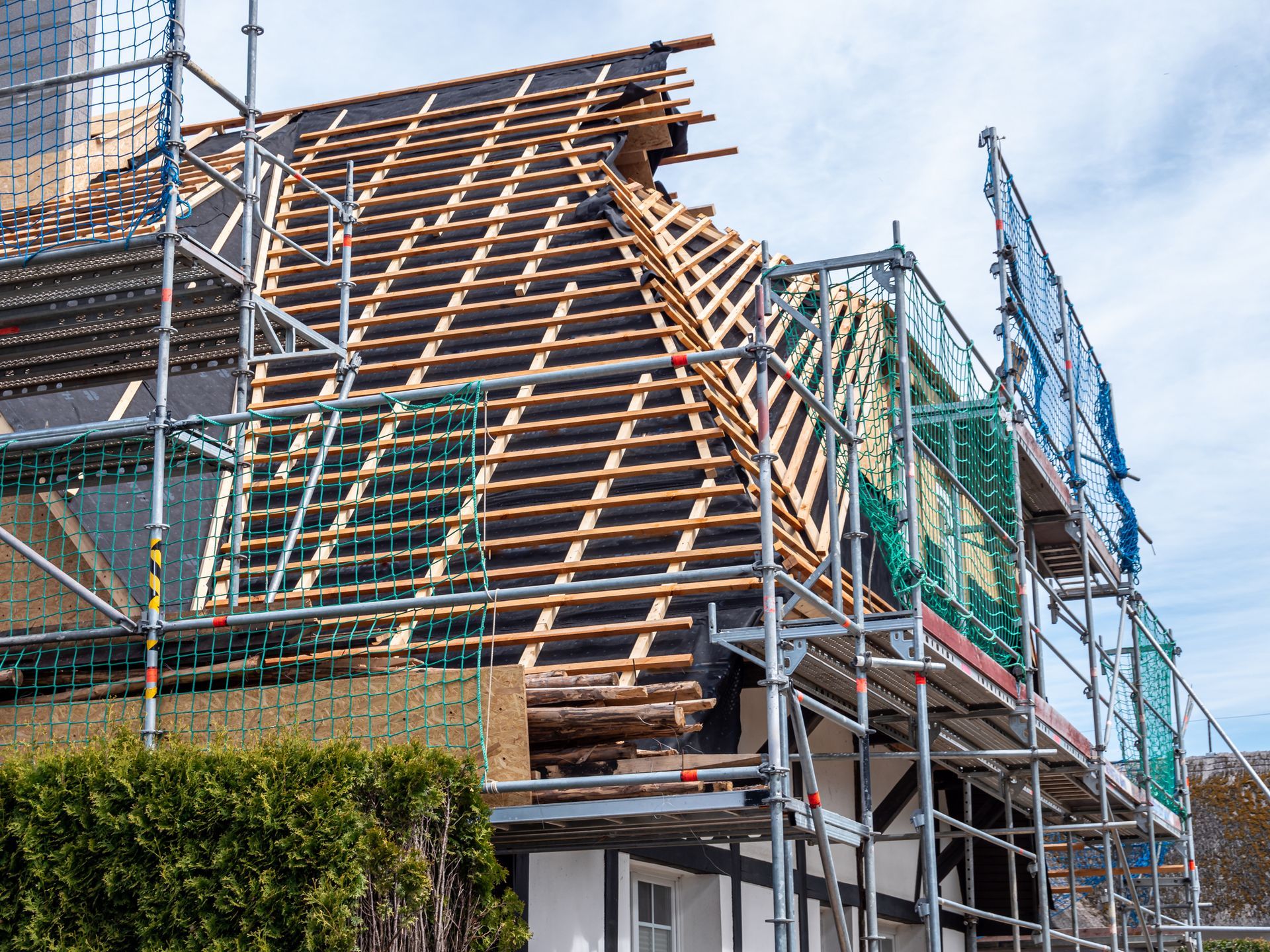 Roof of a building under construction, scaffolding surrounding the structure, cloudy sky.