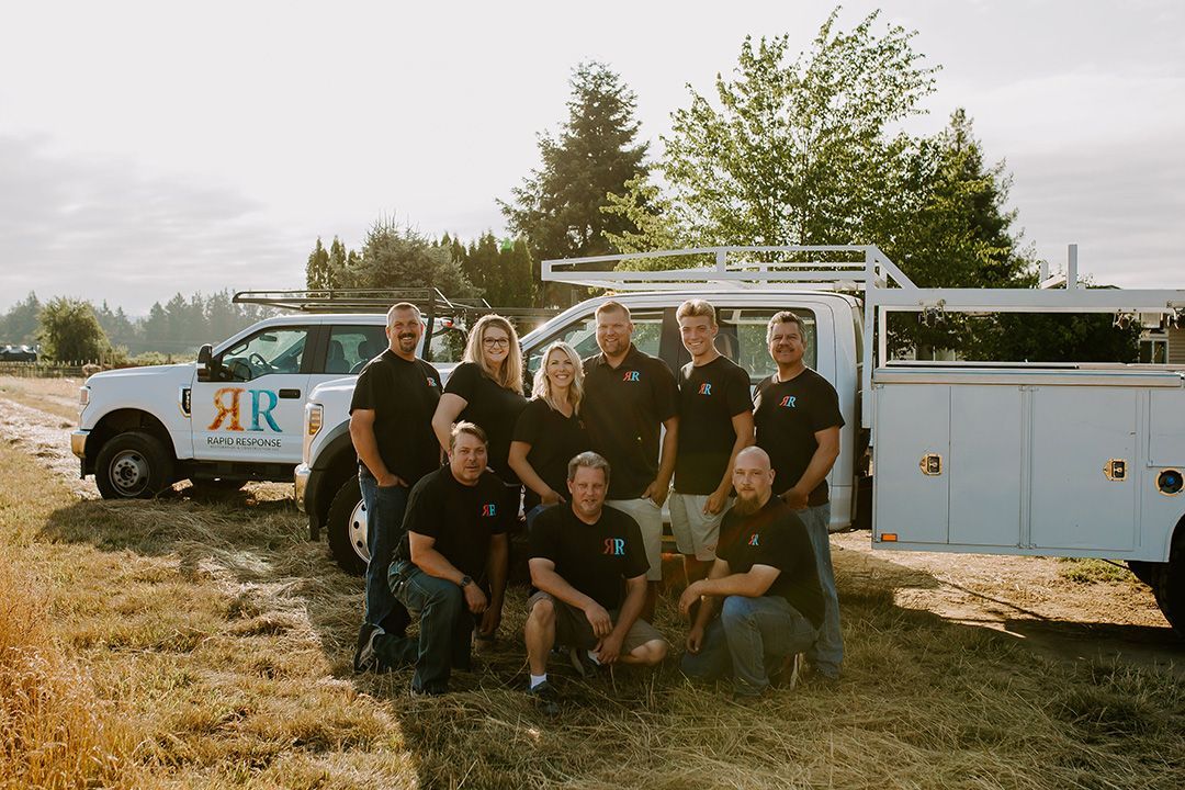 A team of people in black shirts posing in front of two white work trucks, in a field.