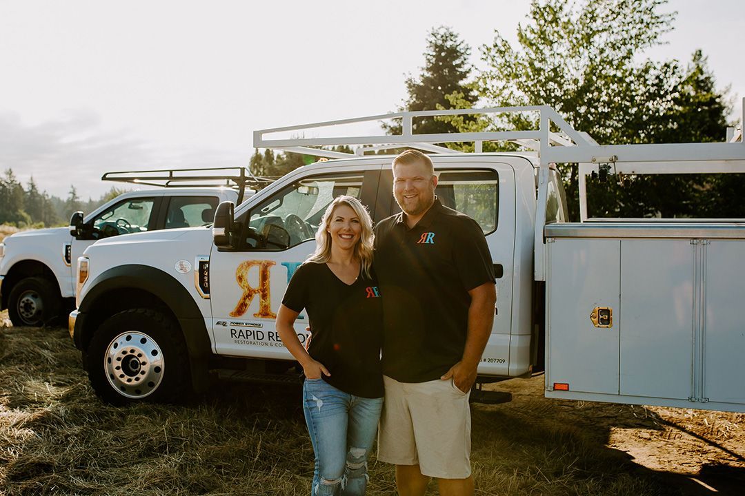 Man and woman standing beside white work trucks in field.