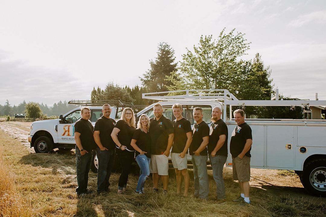 A group of people in black shirts and jeans pose with a white truck outdoors in a field.