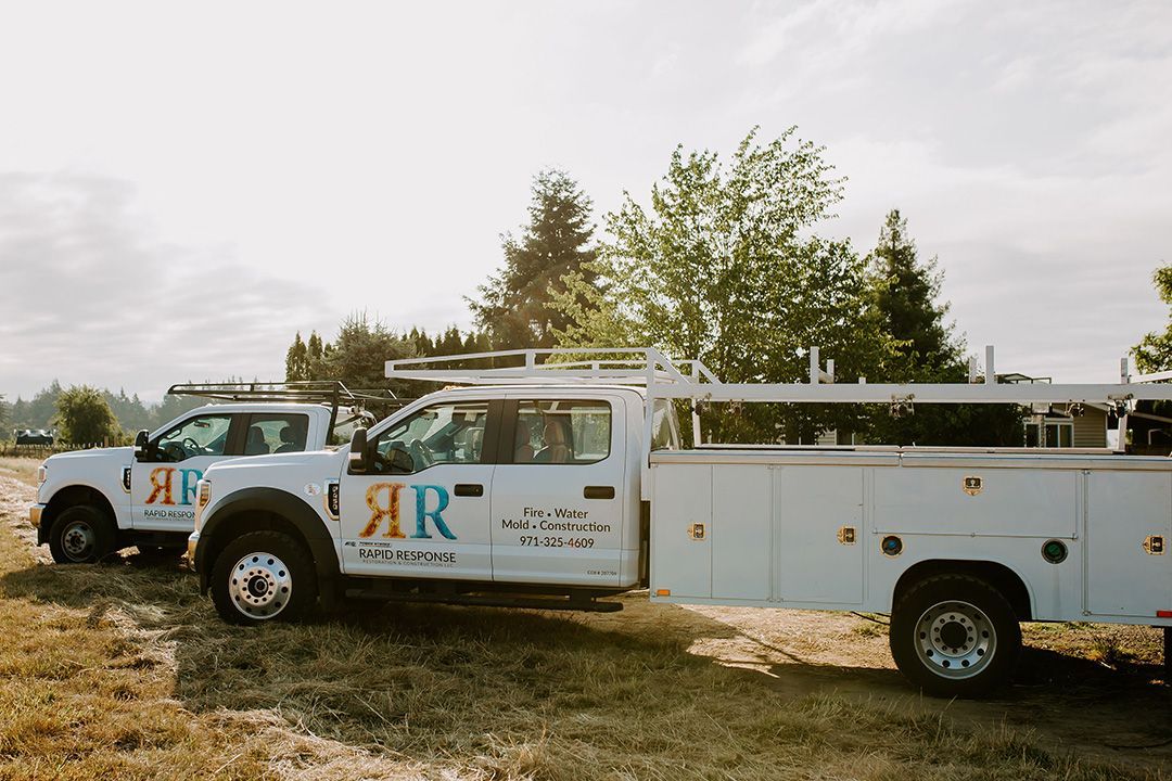 Two white work trucks parked on grass, logo 