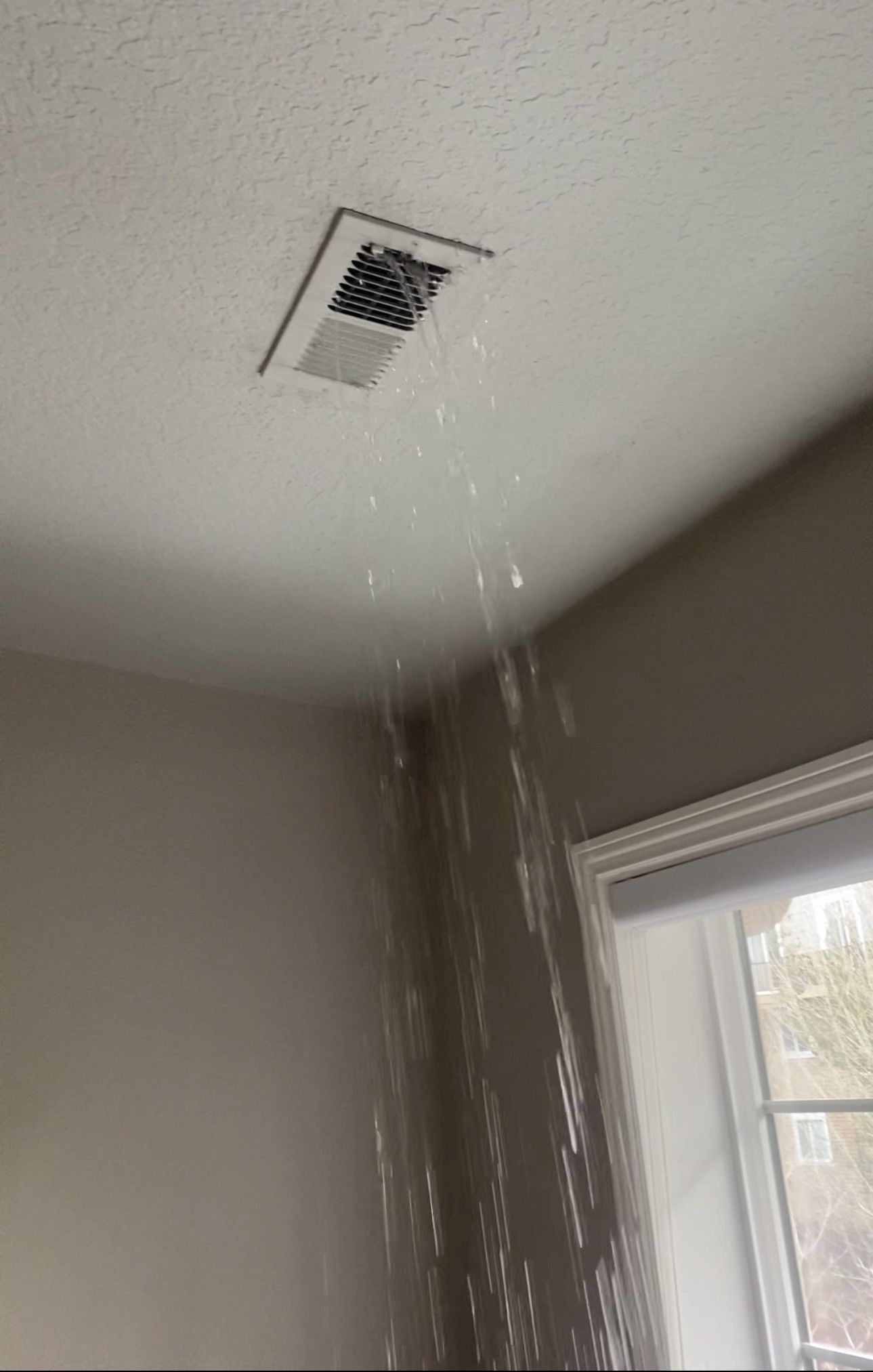 Water gushing from a ceiling vent indoors, near a window.