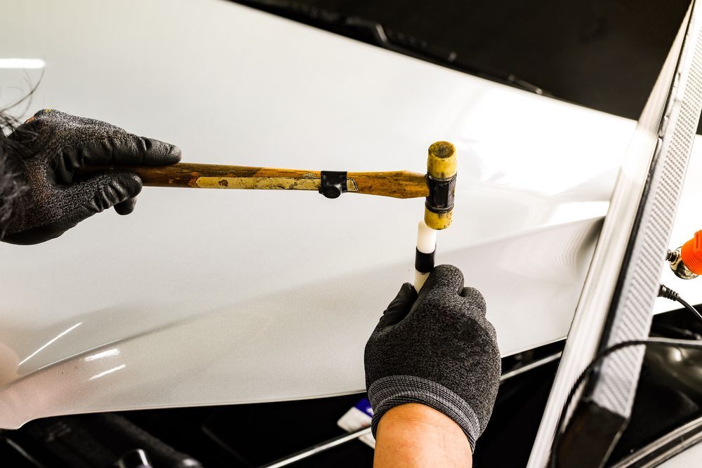 Gloved Hands Using a Mallet on a White Car Panel, Likely Repairing Dents — Forster Smash Repairs in Forster, NSW