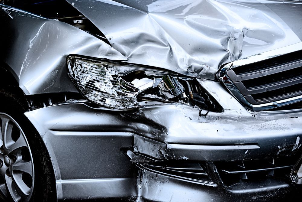 Severe front-end car crash with crushed silver hood and damaged headlight and grille