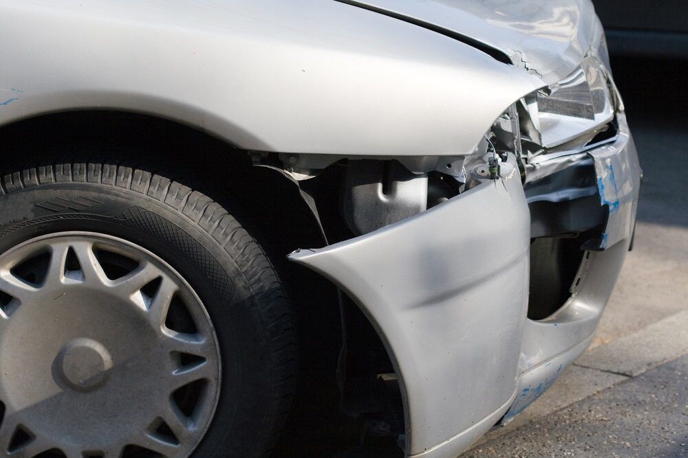 Damaged silver car front bumper and headlight after a collision on a road