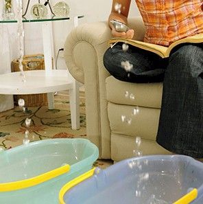Water leaking from ceiling into buckets on a carpet; person on couch, holding a bowl, unaware. Water leaking from ceiling into buckets on a carpet; person on couch, holding a bowl, unaware.