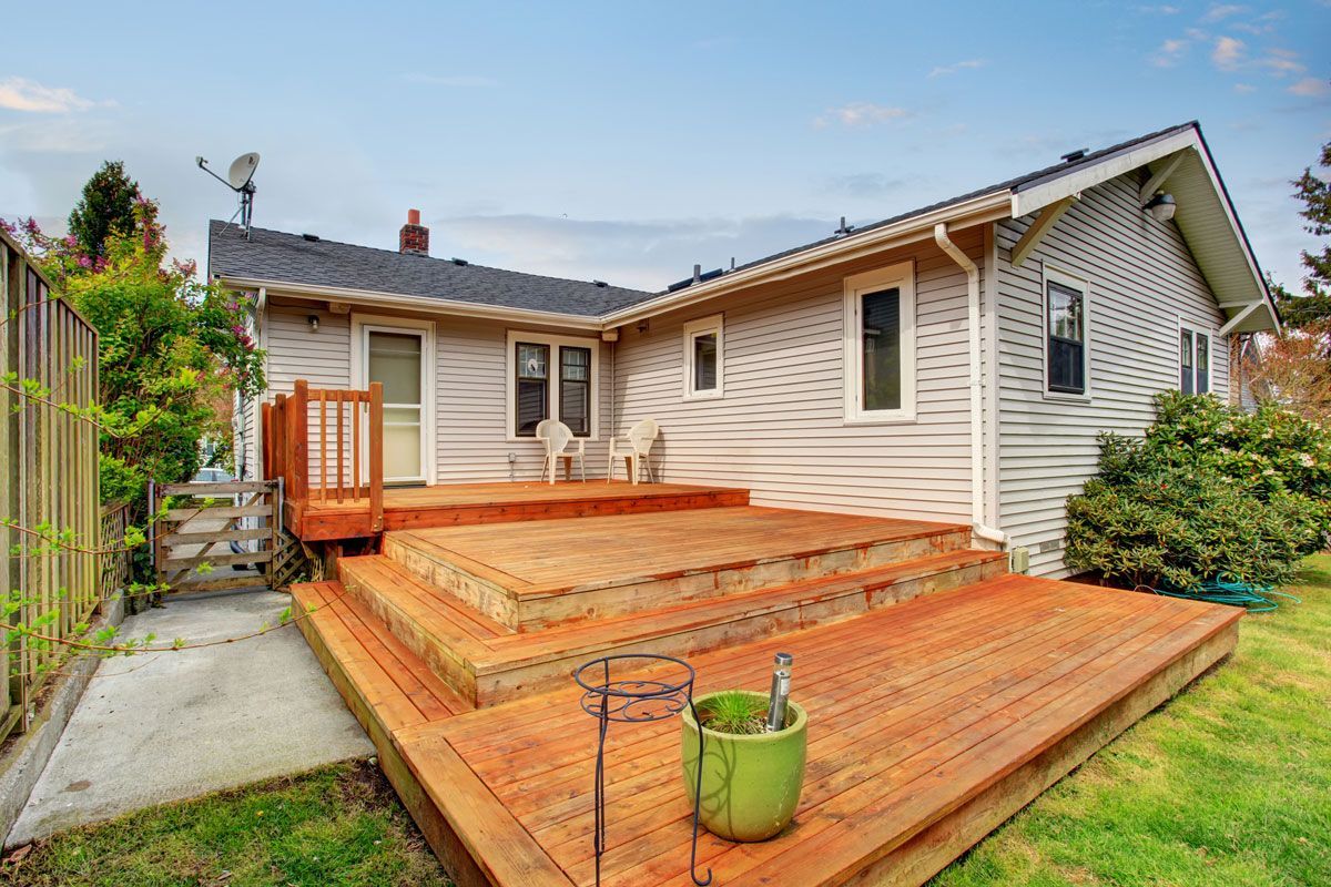 Wooden deck attached to a light-colored house. Green grass and a small green pot in the yard.