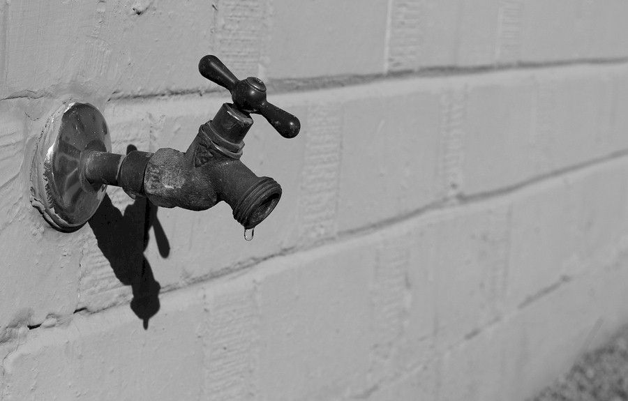 Rusty outdoor water faucet mounted on a painted cinder block wall, dripping water.