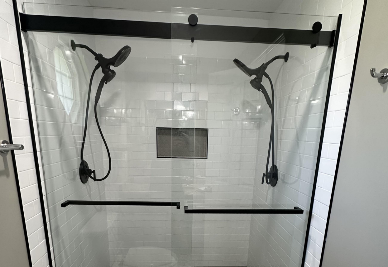 Modern bathroom with a light wood vanity, black fixtures, and a glass shower.