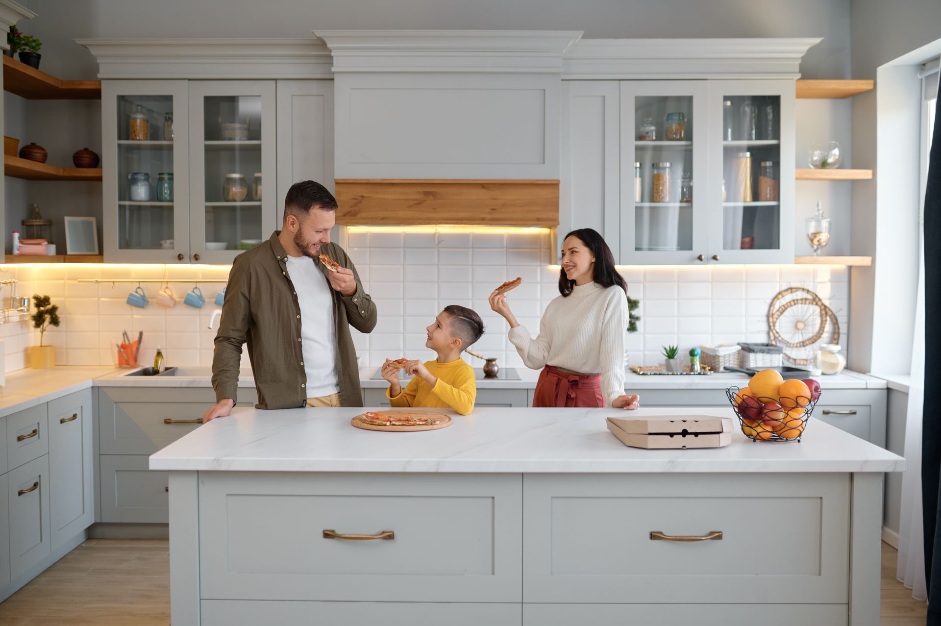 A family is standing in a kitchen with a child sitting on the counter.