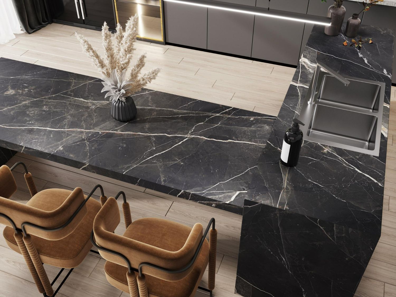 A modern kitchen with black marble countertops, tan chairs, and a vase of dried flowers.