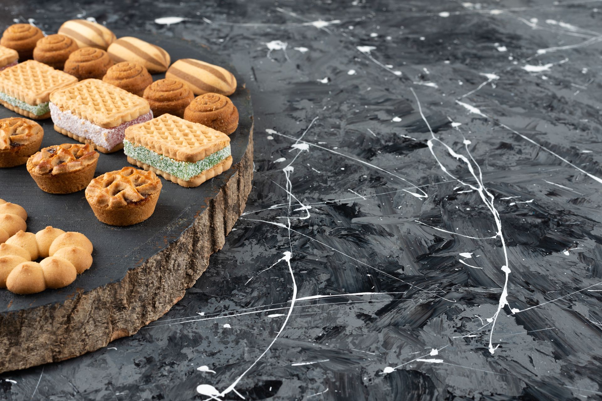 Cookies and pastries on a wooden slab, set against a speckled, dark gray surface.