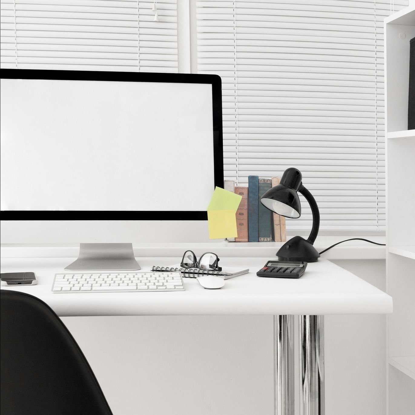 A white desk with a computer , keyboard , lamp , and shelves.