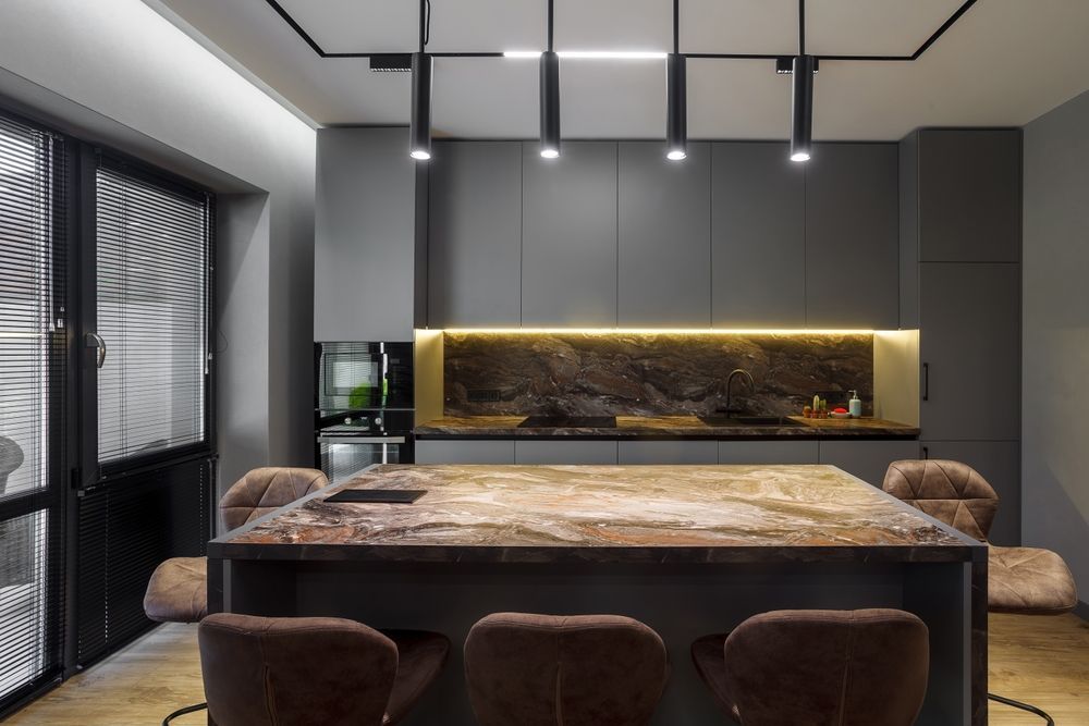 Modern kitchen with dark gray cabinets, a stone countertop, and a large island with brown seating.