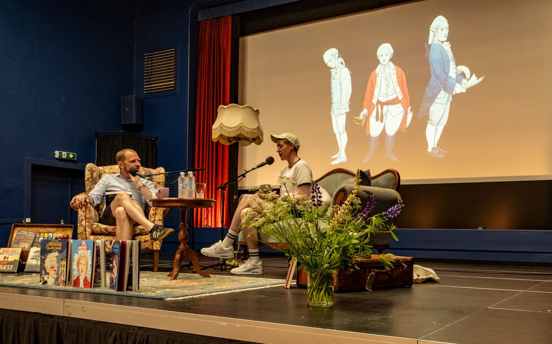 To mænd sidder på en scene foran en stor skærm.