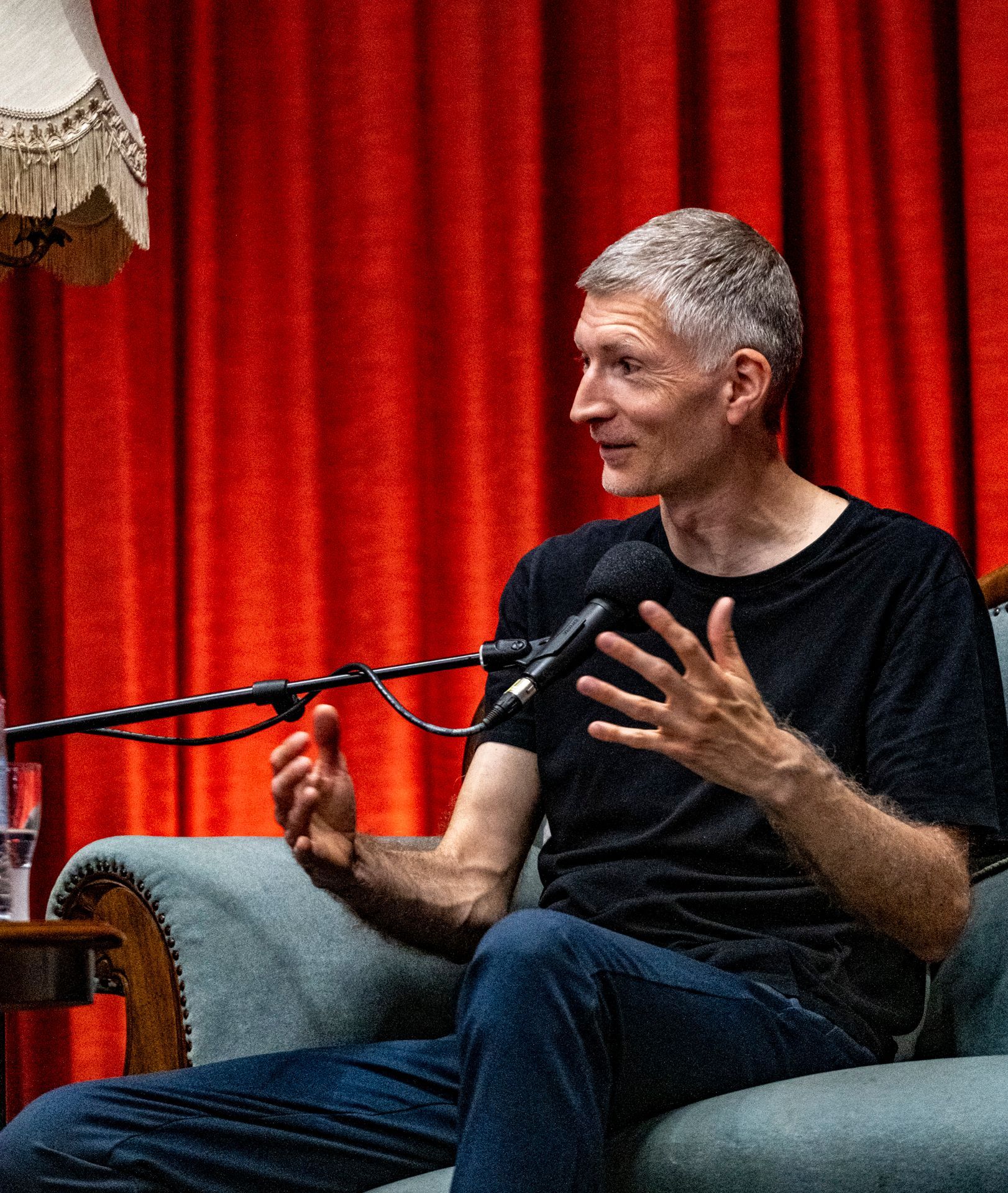 En mand sidder foran en mikrofon foran et rødt gardin.