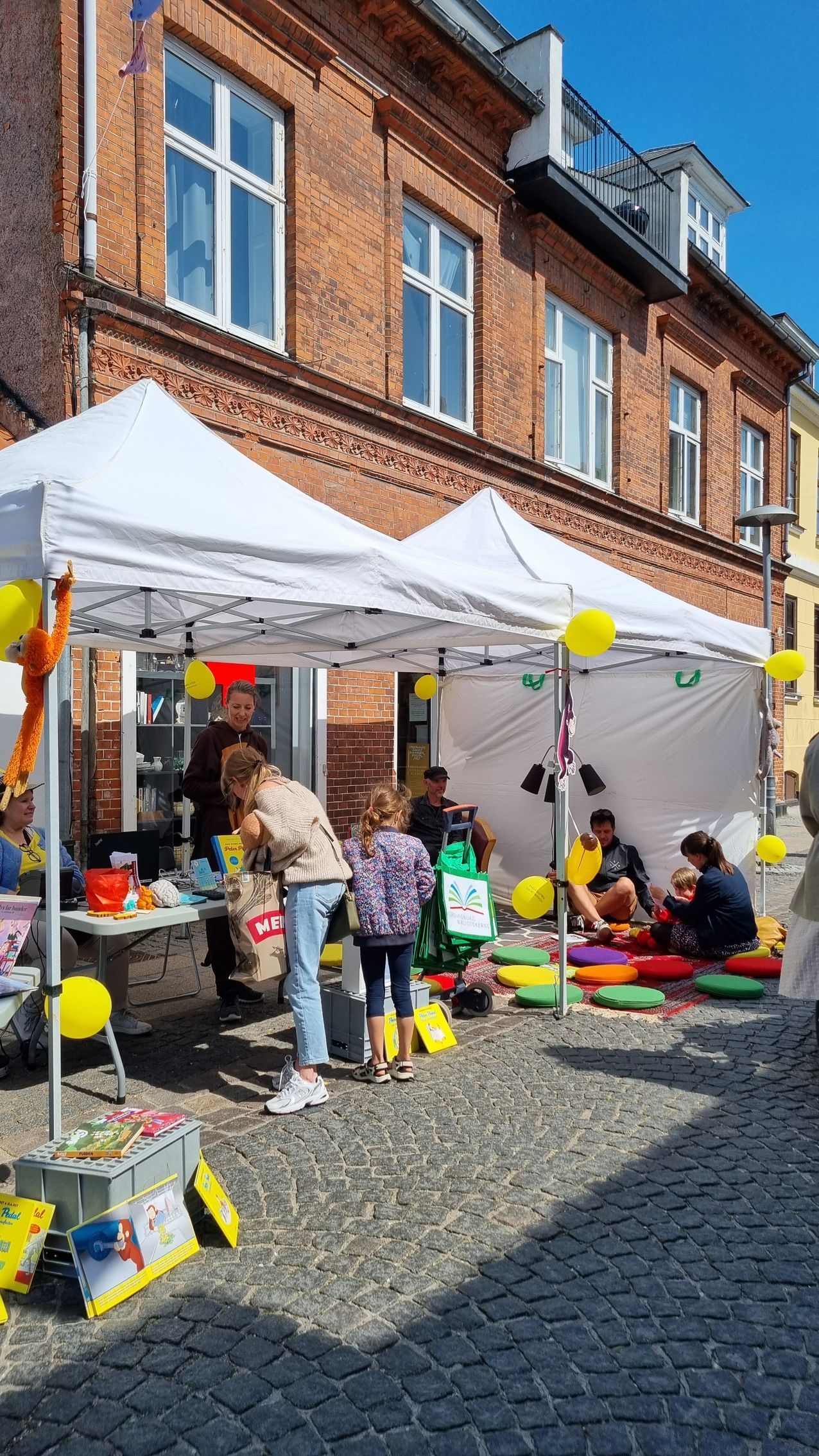 En gruppe mennesker står under telte foran en murstensbygning.