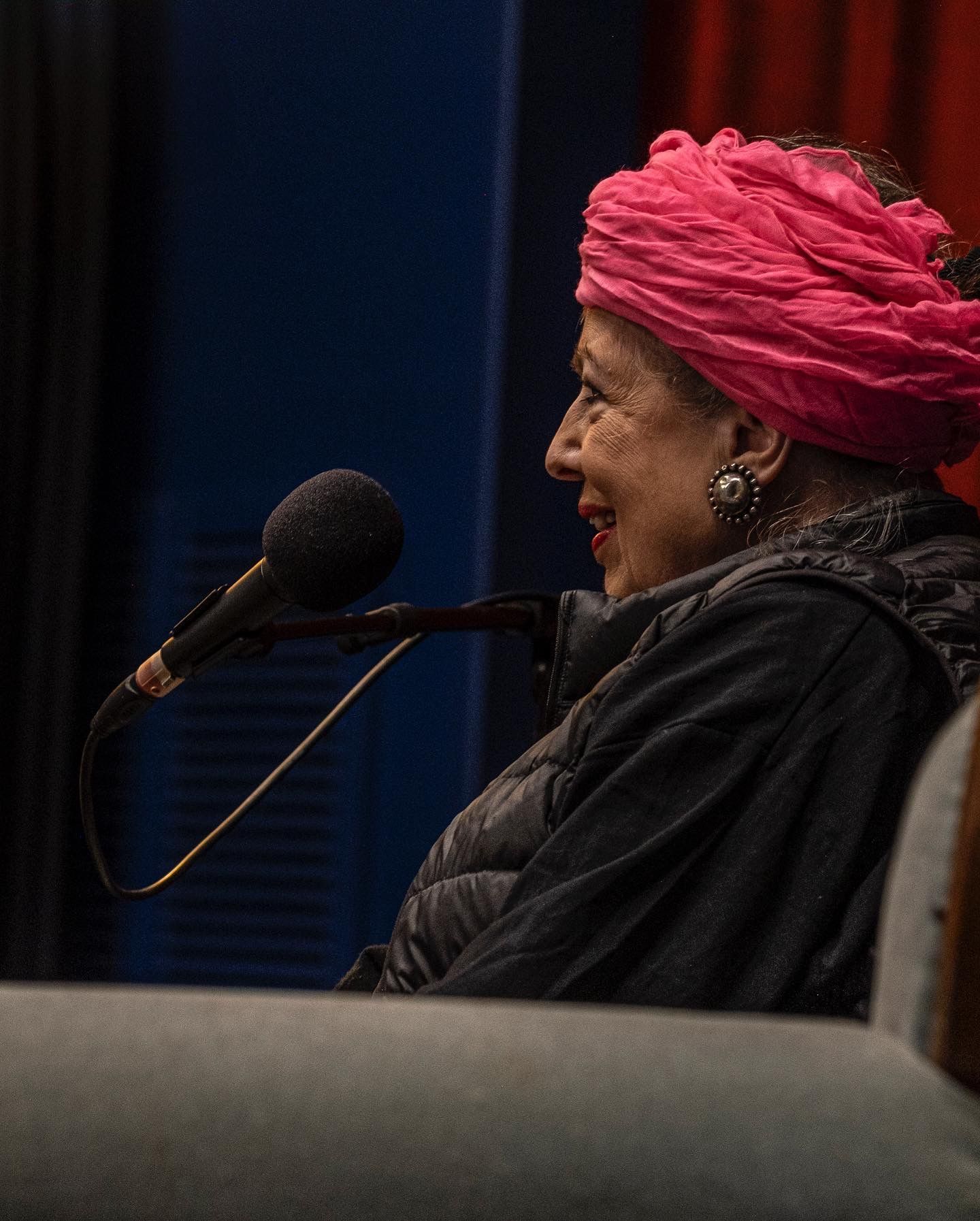 Suzanne Brøgger iført en lyserød turban sidder foran en mikrofon.
