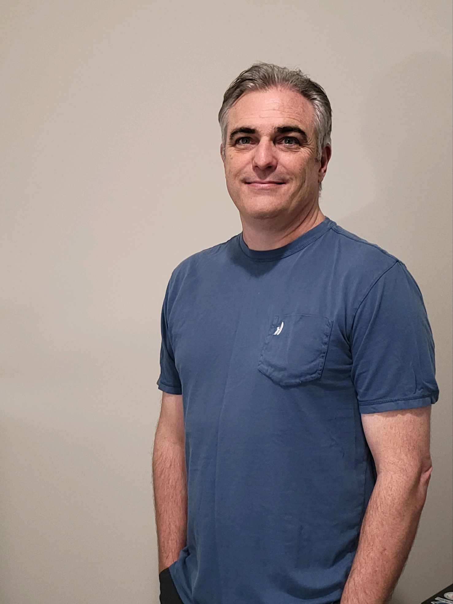 A man in a blue t-shirt is standing in front of a white wall.
