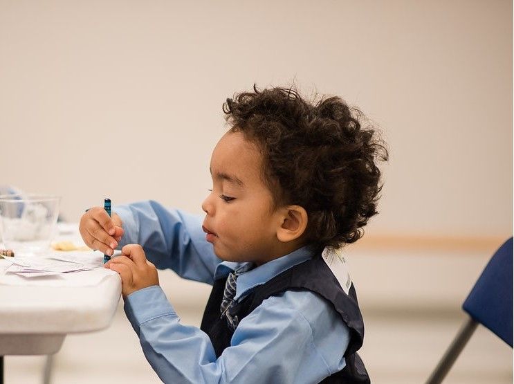 A young boy is sitting at a table with a marker in his hand.