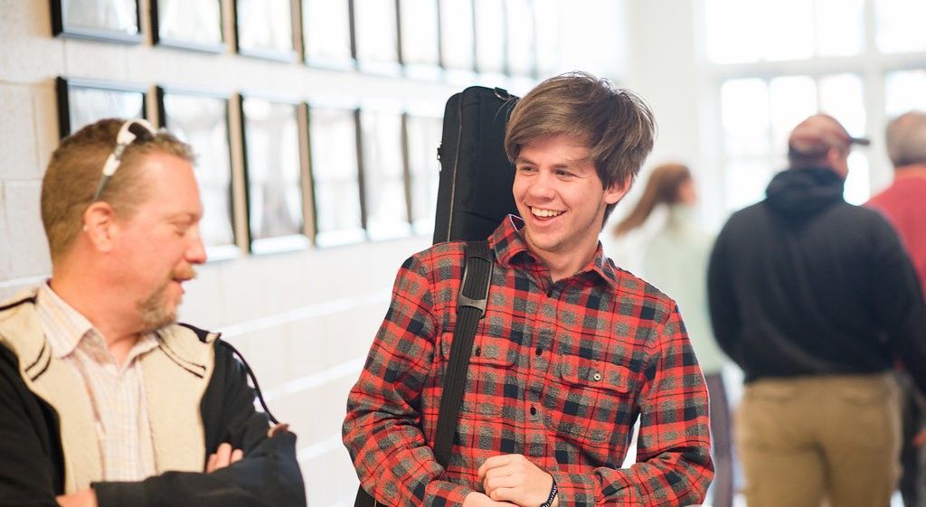 A man in a plaid shirt is talking to another man in a hallway.