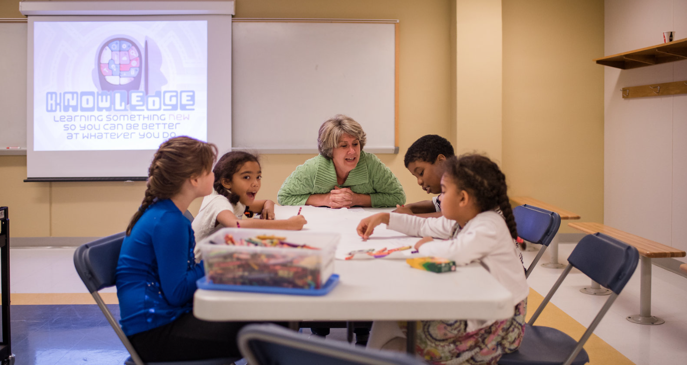 A group of children are sitting around a table in a classroom.