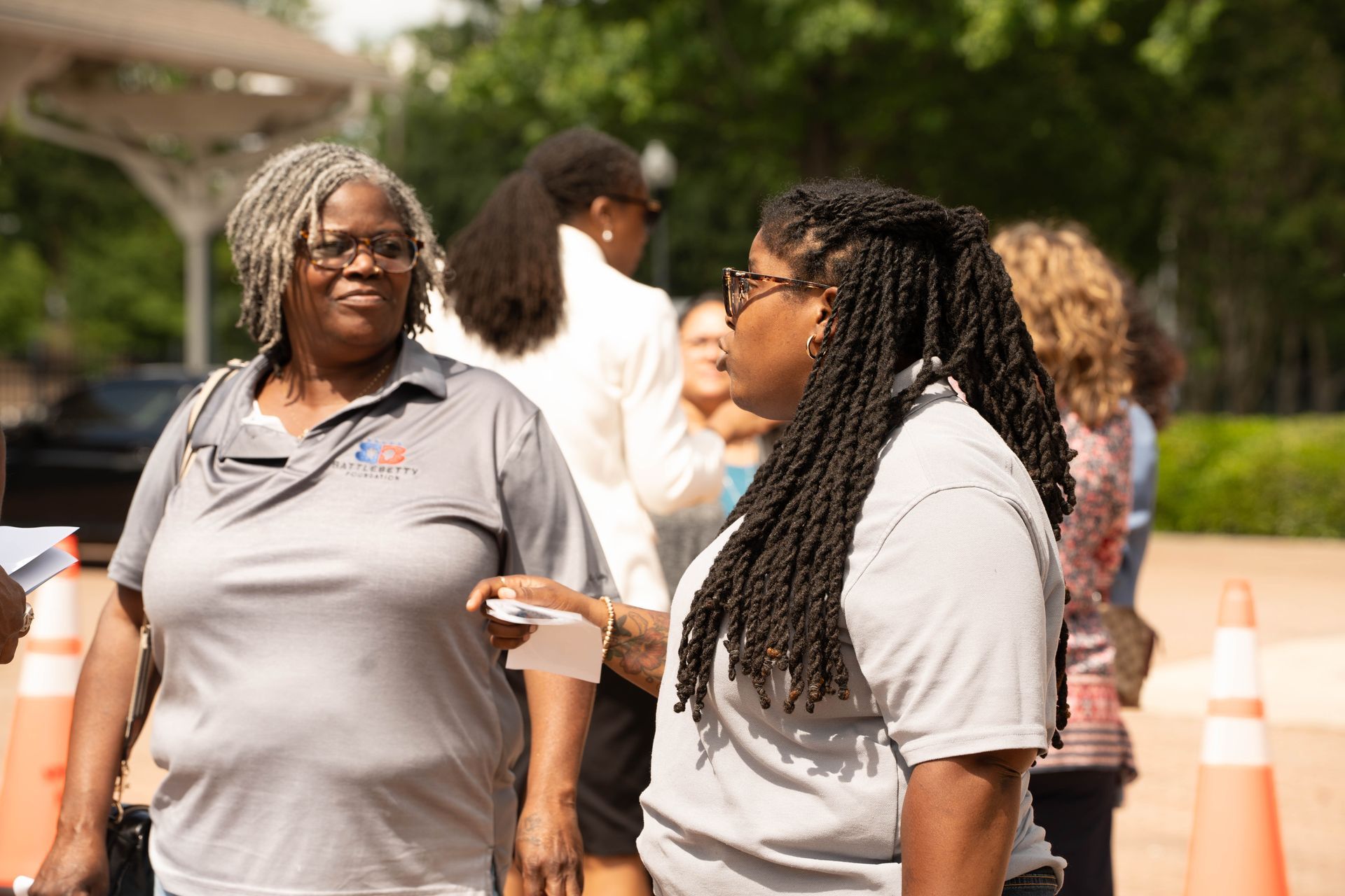 Two women talking outside; one with gray dreads, the other wearing glasses.