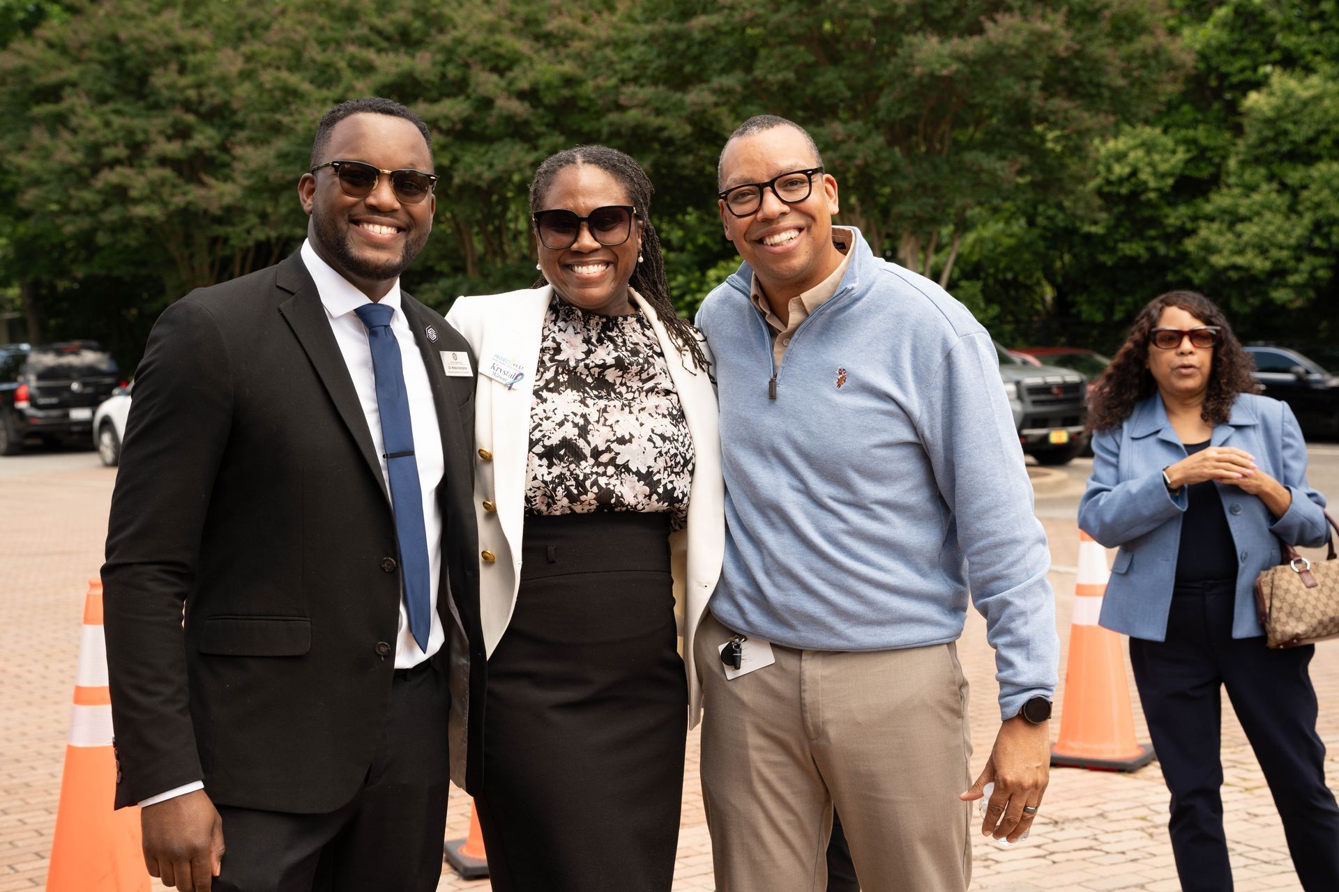 Three people smiling, posing outside; man in suit, woman in blazer, man in polo.
