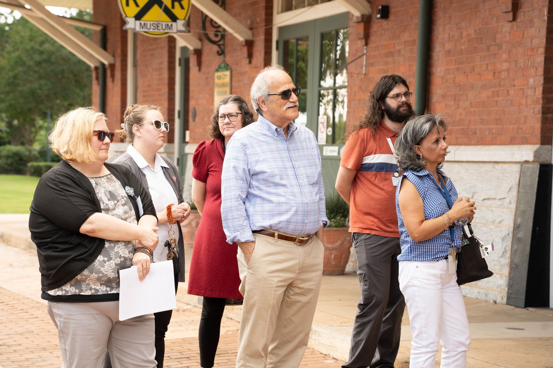 Group of people standing outside a brick building, possibly a museum.