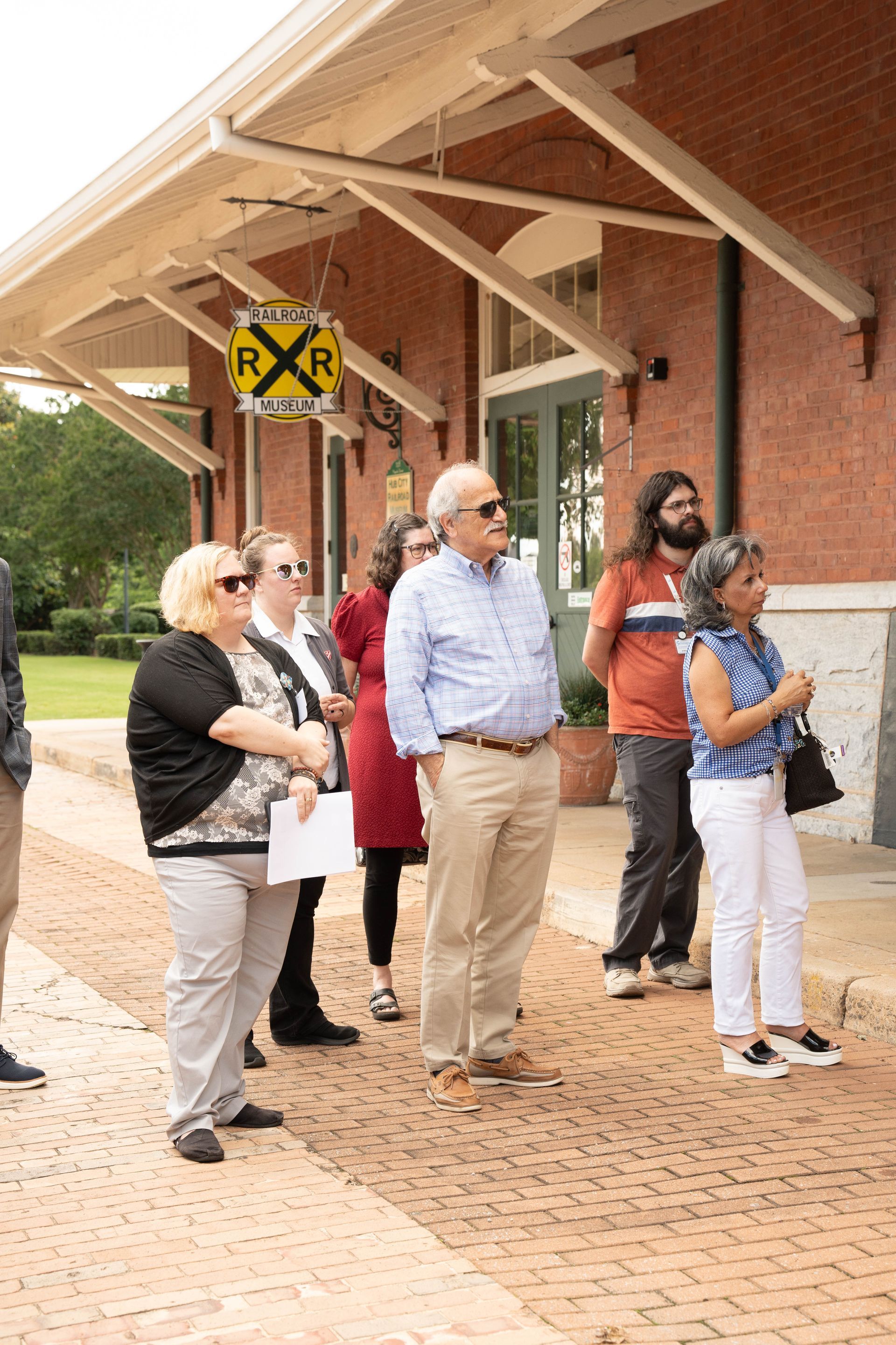 Group of people standing on a brick platform under a building overhang, looking forward.