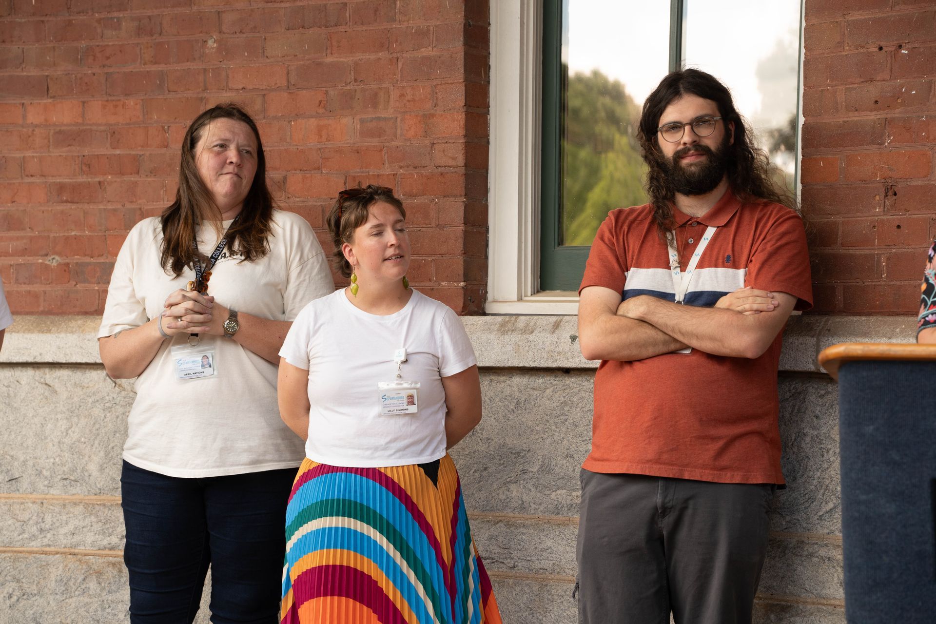 Three people stand outside a brick building: two women and a man with a beard.