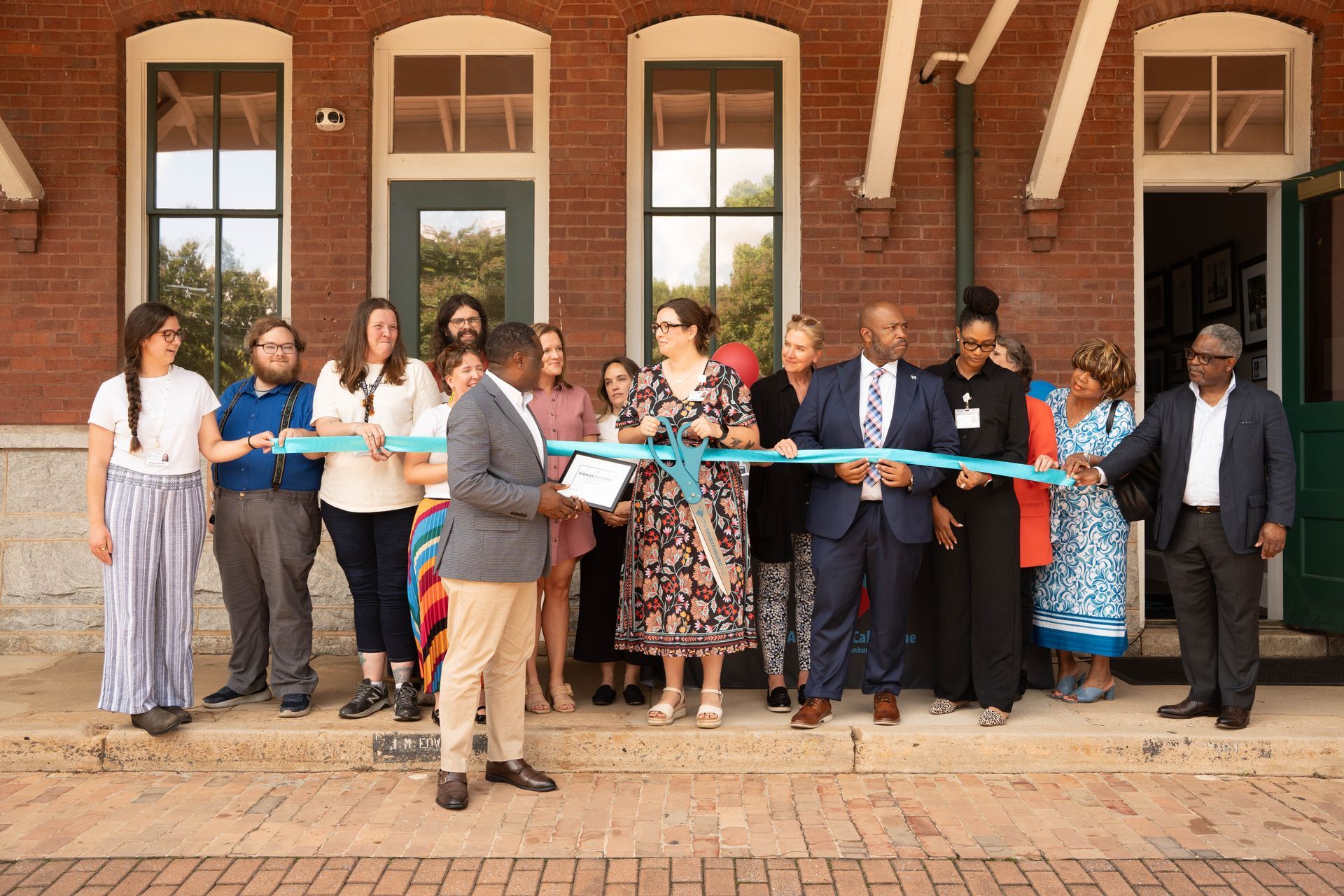 People cutting a ribbon at the opening of a brick building with many windows.