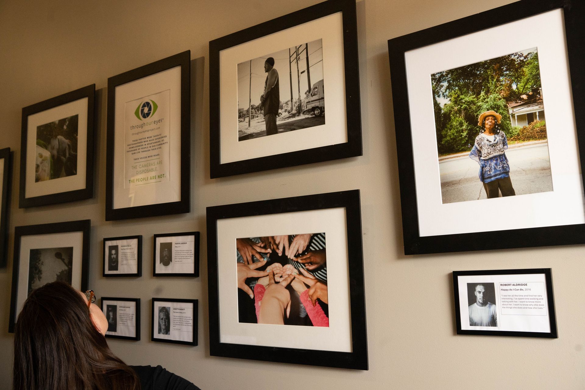 Woman looks at a wall with framed photos of various sizes and subjects.