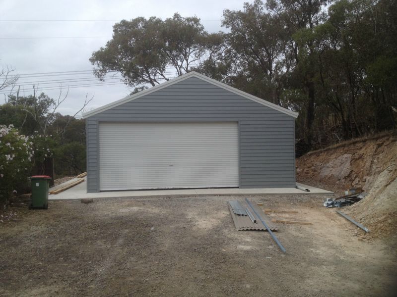A Garage with a White door is Sitting on Top of a Dirt Hill - Wallan, VIC - Victorian Garages & Barns
