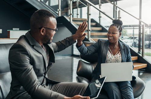 A man and a woman are giving each other a high five while sitting on a couch with a laptop.