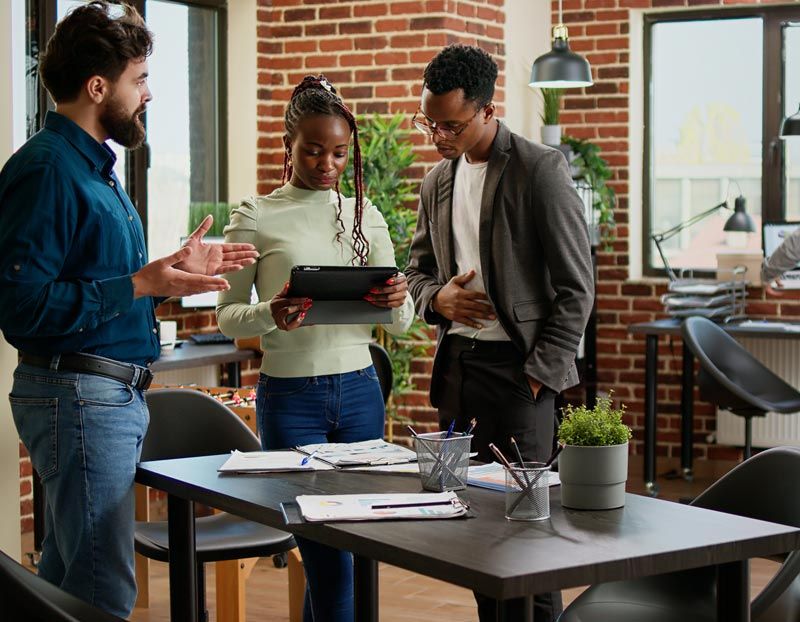 A group of people are standing around a table looking at a tablet.
