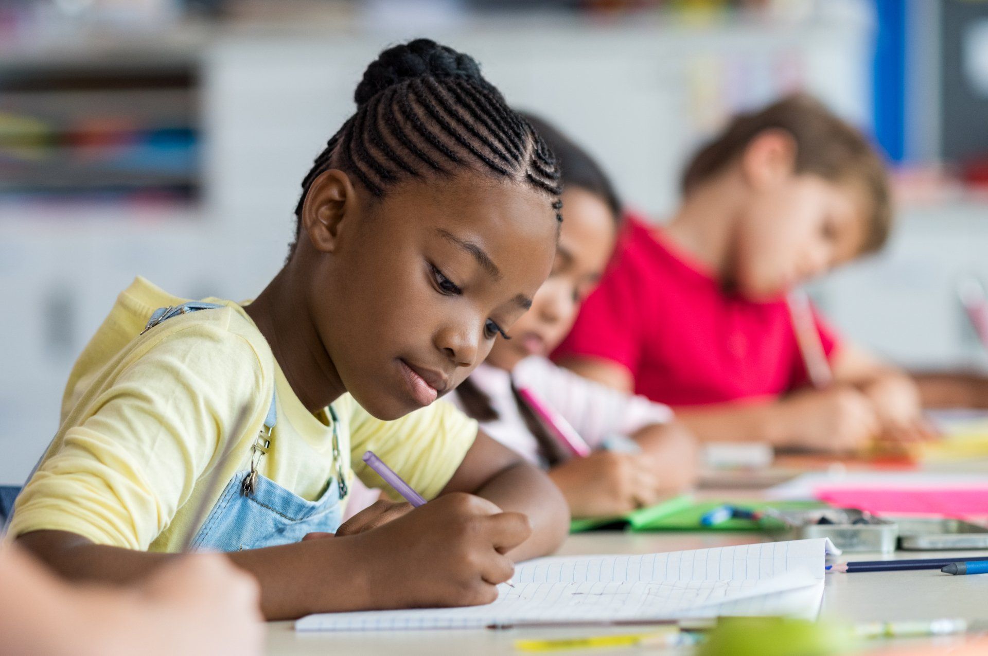 A group of children are sitting at desks in a classroom writing in notebooks.