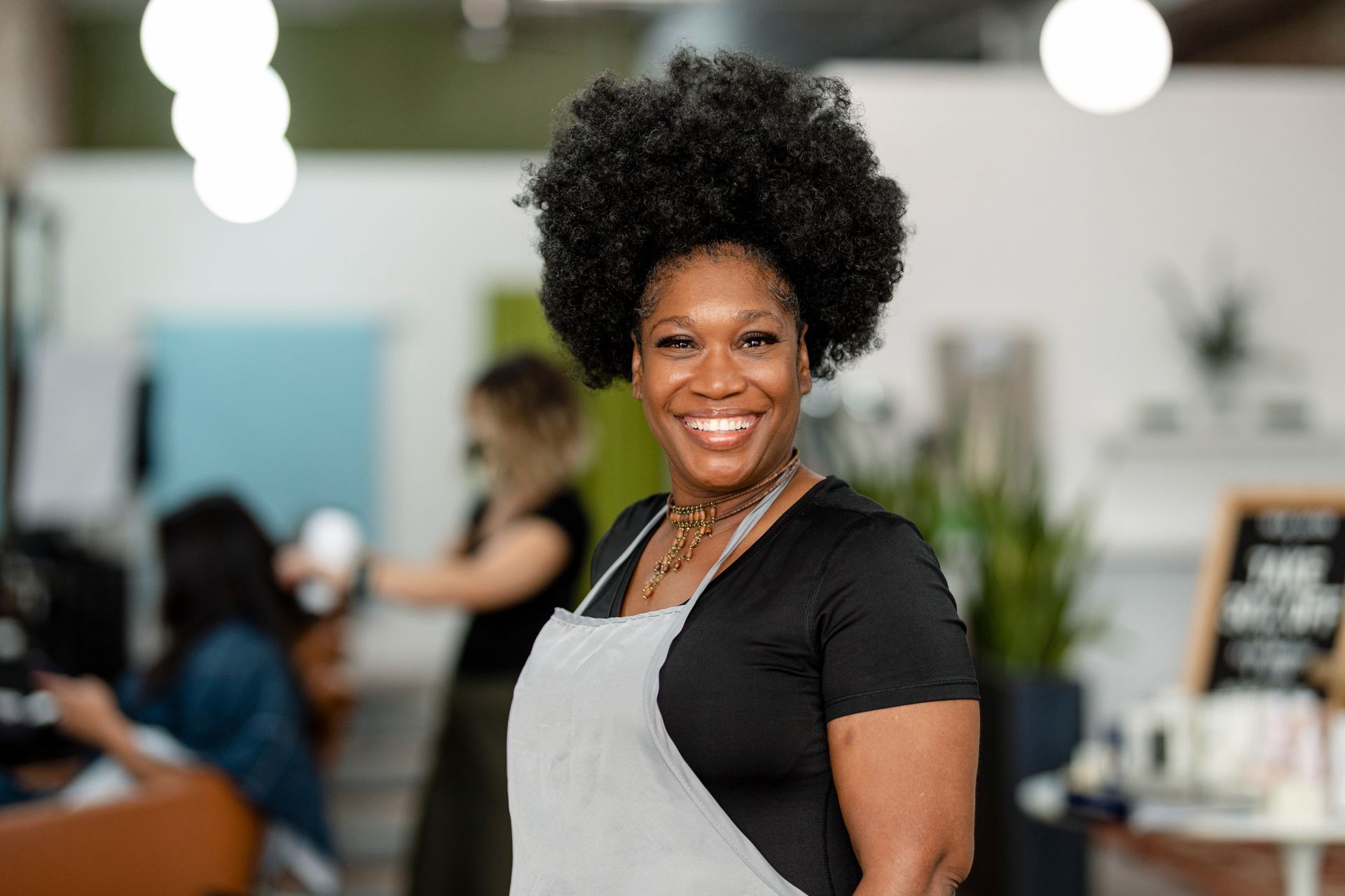 A woman is wearing an apron and smiling in a salon.
