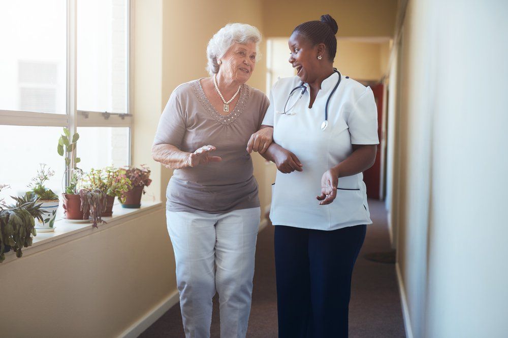 A nurse is helping an elderly woman walk down a hallway.