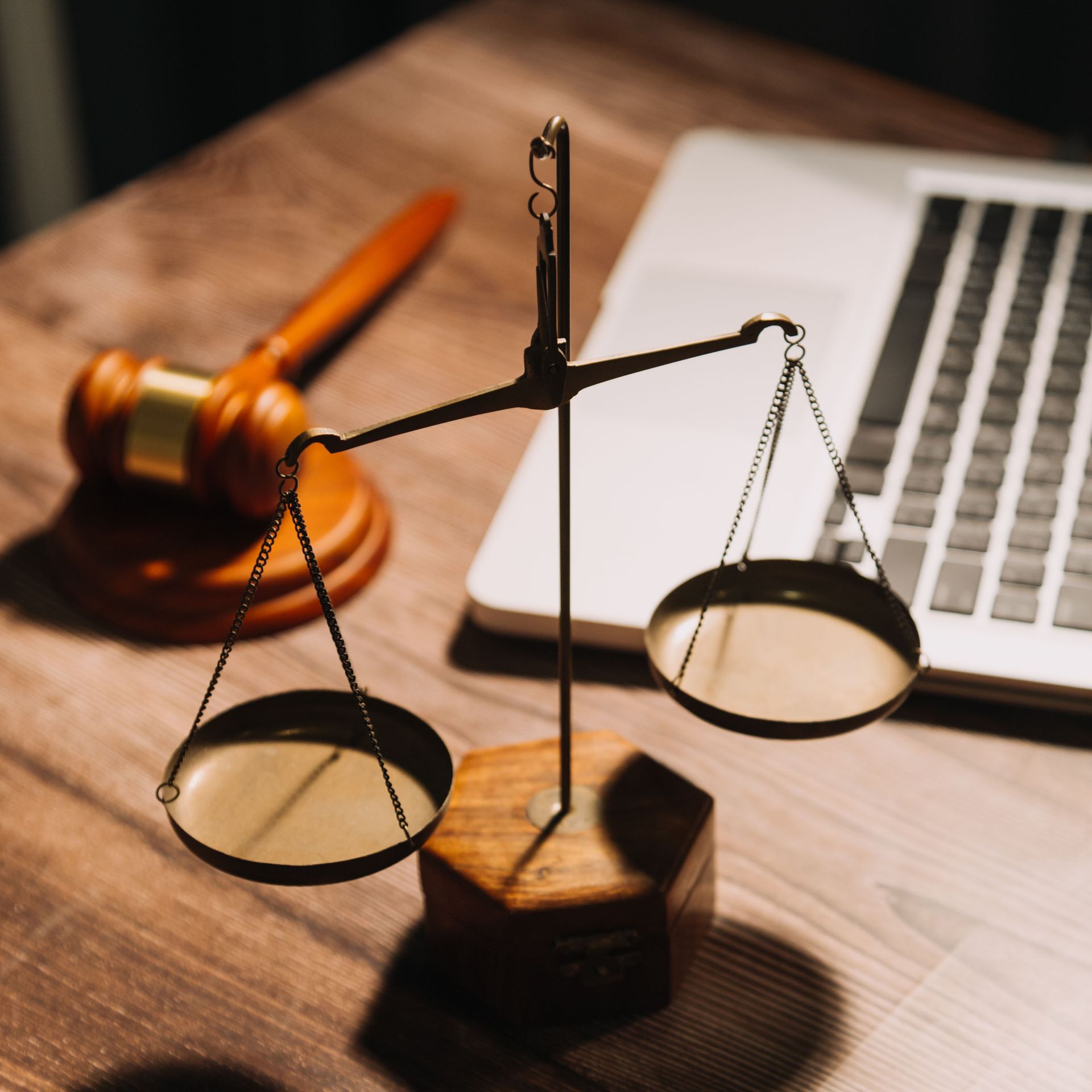 A scale of justice sits on a wooden table next to a laptop