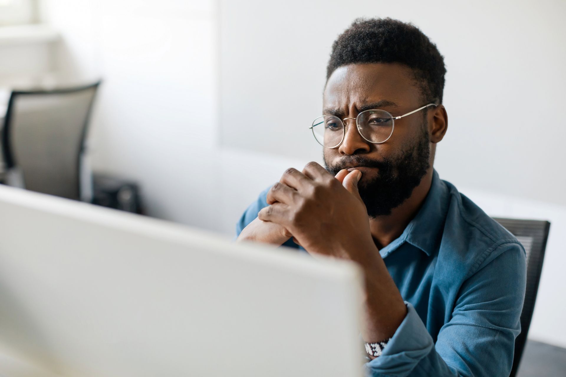 Man with glasses and beard, biting nails, looking intently at a computer screen.