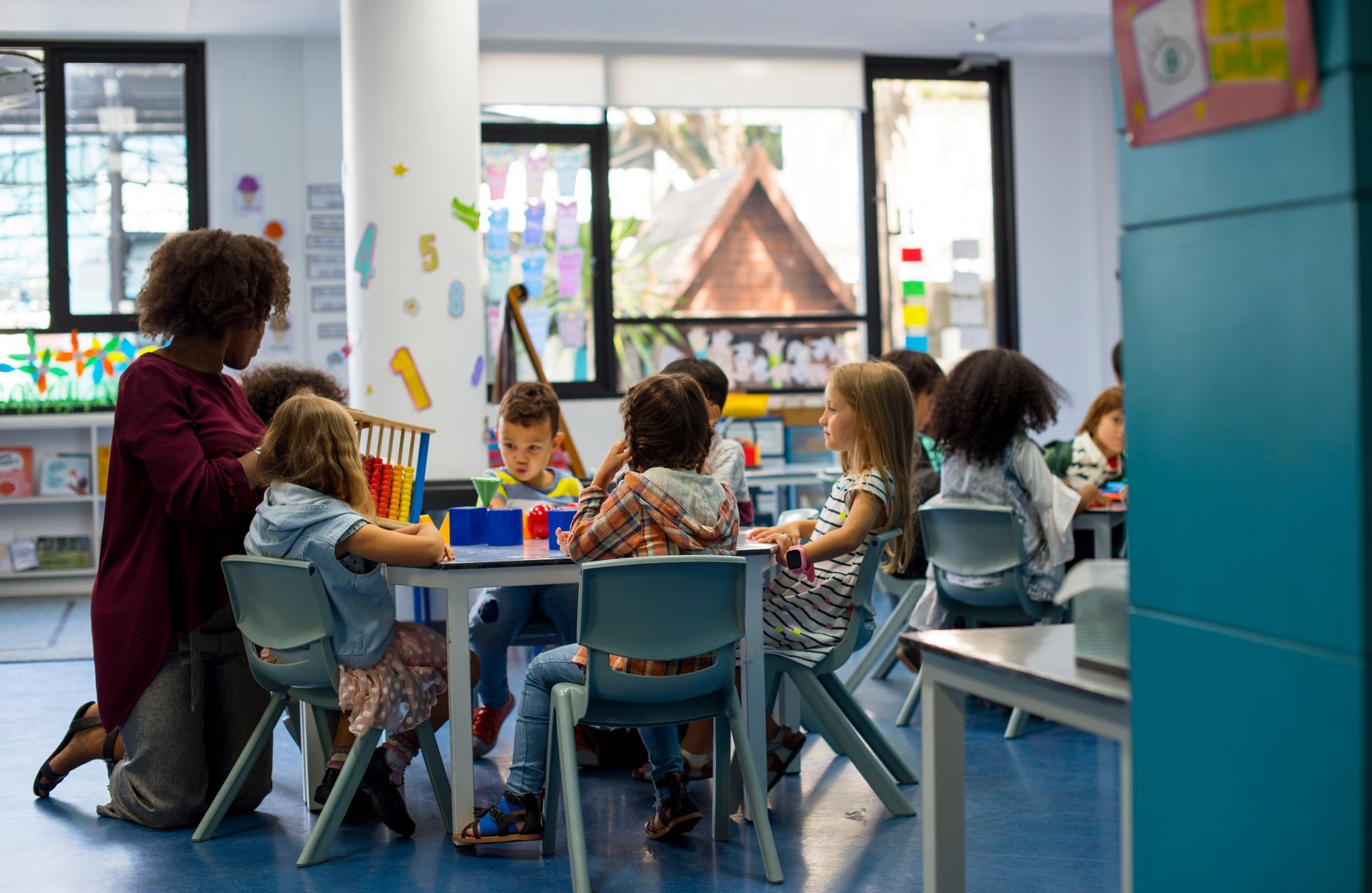 A group of children are sitting at tables in a classroom with a teacher.