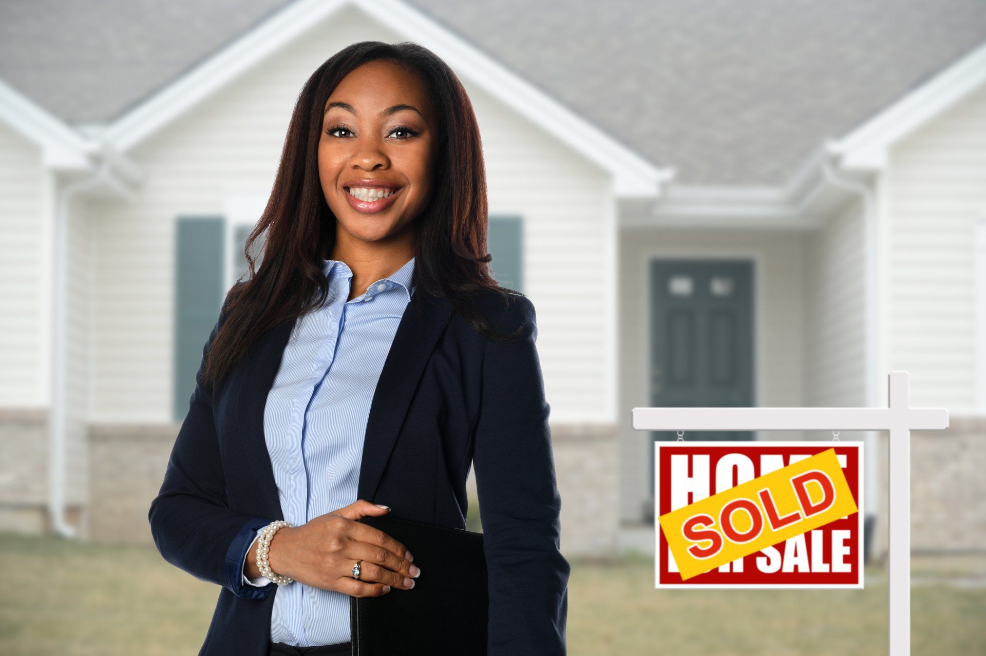 A woman is standing in front of a house with a sold sign in front of her.