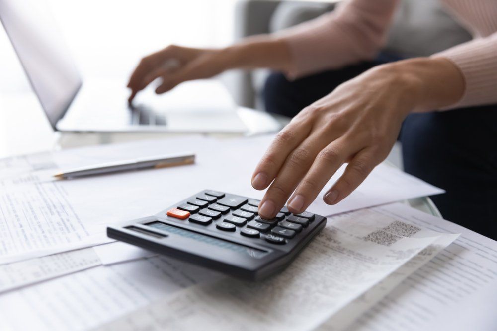 A person is using a calculator while typing on a laptop.